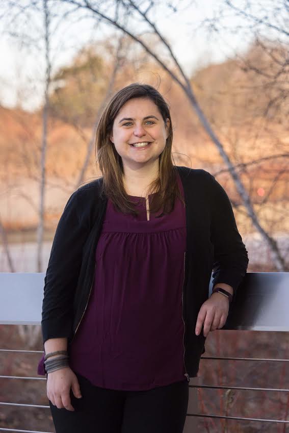 Smiling woman standing outdoors, in autumn (no leaves on the deciduous trees in the background)