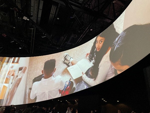 View of a large projected video on a wall with children in classrooms as the subject.