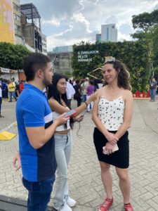 A woman speaks into a small microphone held by a young woman, while a young man consults questions on his phone