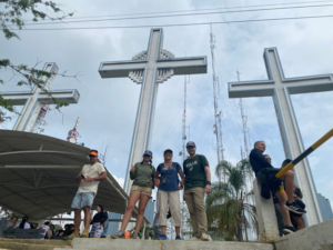 Hikers standing together at the summit of “The Three Crosses” (Las Tres Cruces). They are smiling and dressed in outdoor hiking gear, with a scenic mountain backdrop.