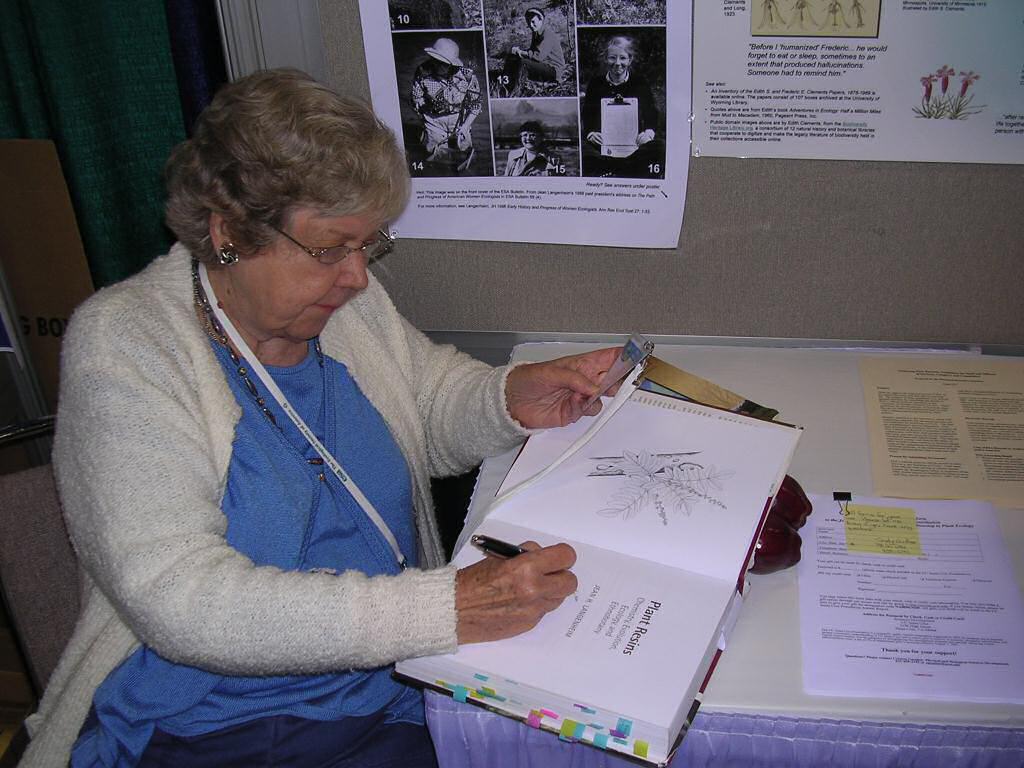 A woman, Jean Signs, signs a copy of her book.