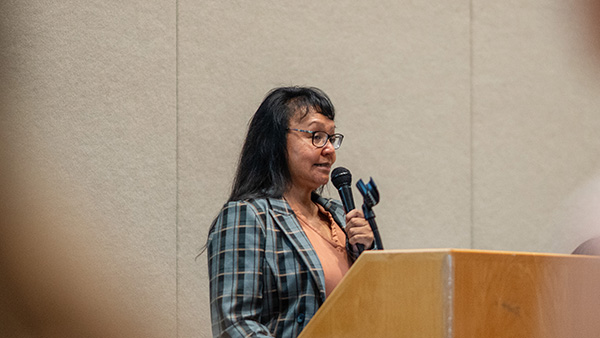 A presenter speaks from a podium holding a microphone in her hand.