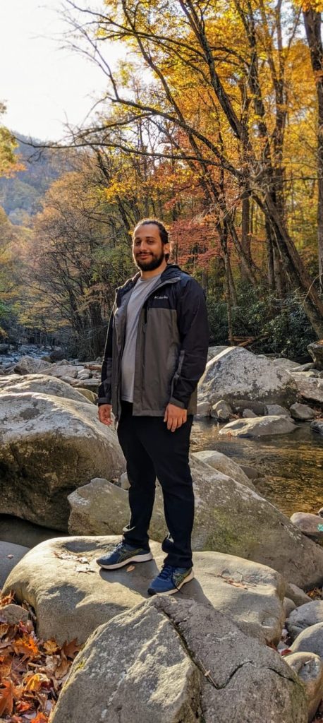 Guido Herrera-Rodriguez poses on a rock in a forest in the background.