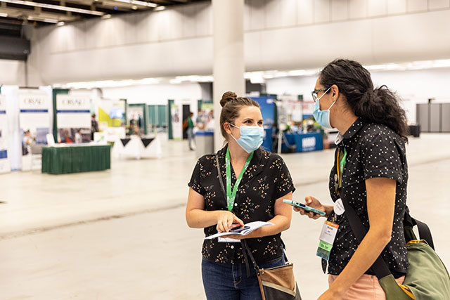 Two attendees chat in the exhibit hall near the poster sessions and exhibitors.