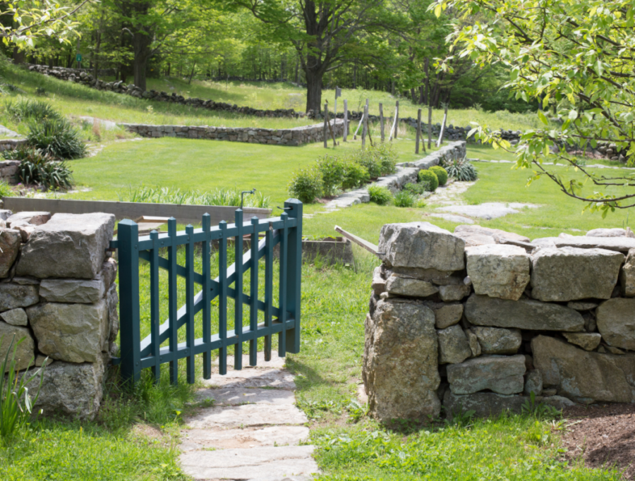 Photo of an open gate connected to a stone wall. The other side of the gate shows a grassy park.